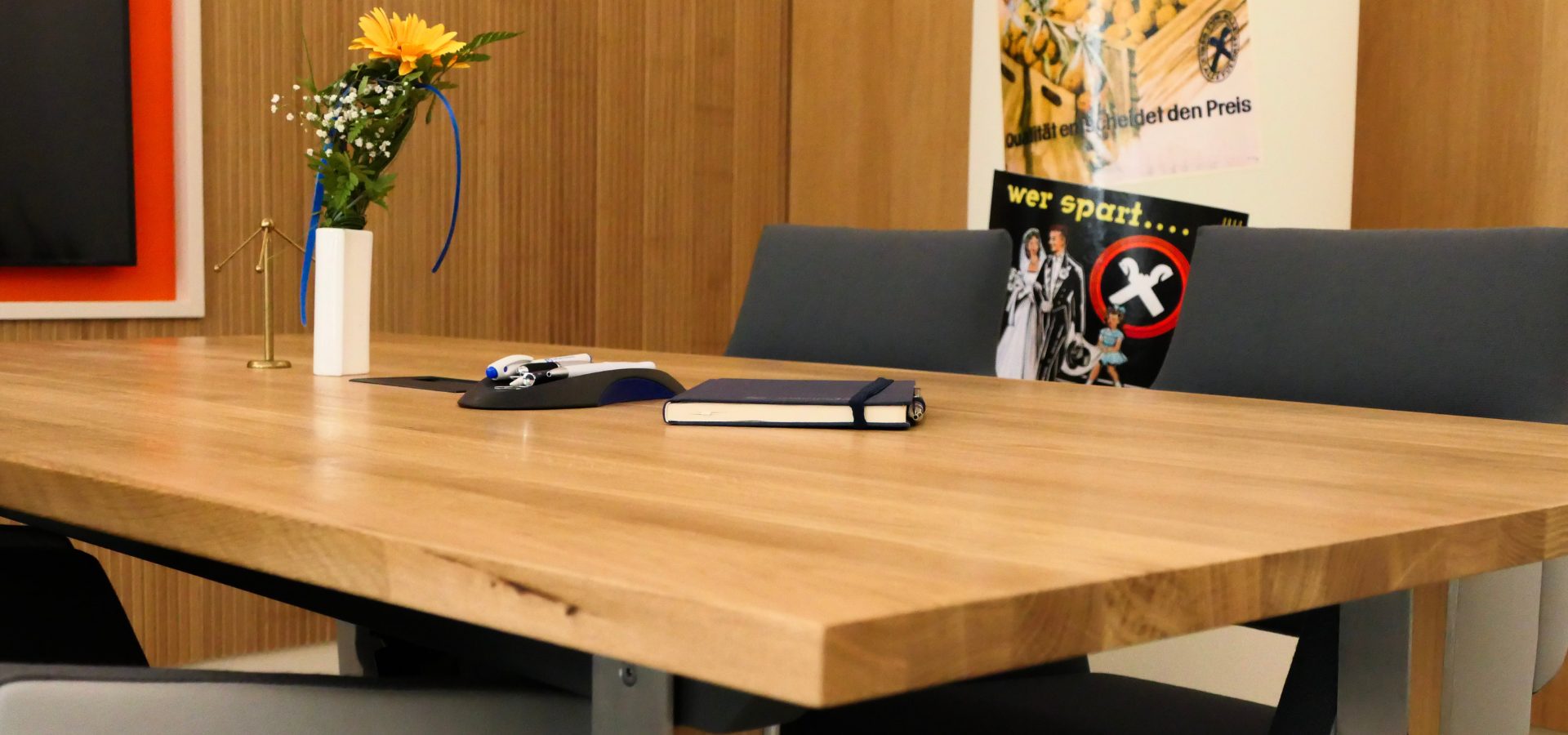 Auf einem Konferenz-Massivholztisch steht eine dekorative Blume sowie Notizbücher.