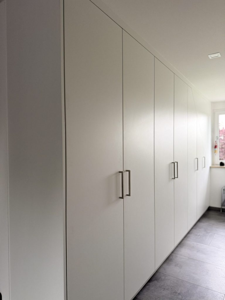 Maßgefertigter weißer Einbauschrank in Dachschräge mit silbernen Griffen – platzsparende Stauraumlösung für moderne Dachwohnungen.