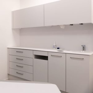 Einbaulösung für eine Arztpraxis mit weißem, durchgehend geschlossenem Schranksystem, integrierter Spüle und hygienischem Abfallsystem; klar strukturierte, griffschlanke Fronten für einen sauberen, professionellen Eindruck.