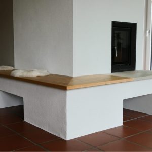 Sitzbank aus Eichenmassivholz am Kachelofen im Wohnzimmer; natürliche Holzoberfläche bringt zusätzliche Wärme und Behaglichkeit in den Raum.