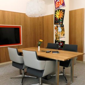 Warm und modern gestalteter Besprechungsraum mit Eichenholz an den Wänden, einem großzügigen Massivholztisch und grauen Stühlen.