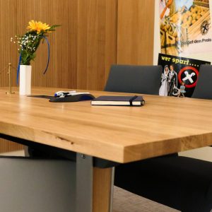 Stilvolles Besprechungszimmer mit Wandpaneelen aus schmalen Eichenstreben, einem großen Massivholztisch und grauen Stühlen in warmer Atmosphäre.
