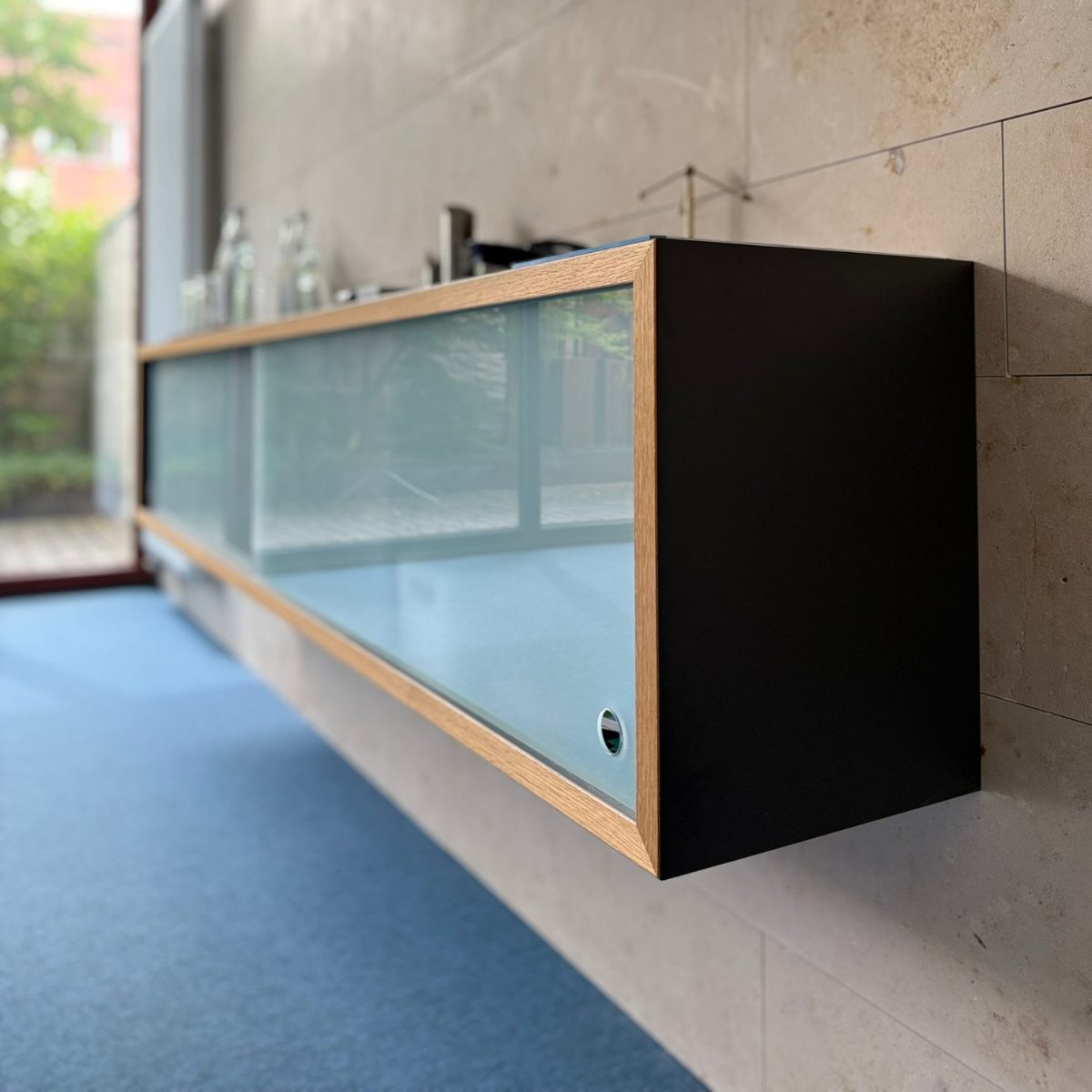 Stilvolles Sideboard aus dunklem Holz, dessen milchige Glasfront dem Möbelstück eine moderne und leichte Optik verleiht.