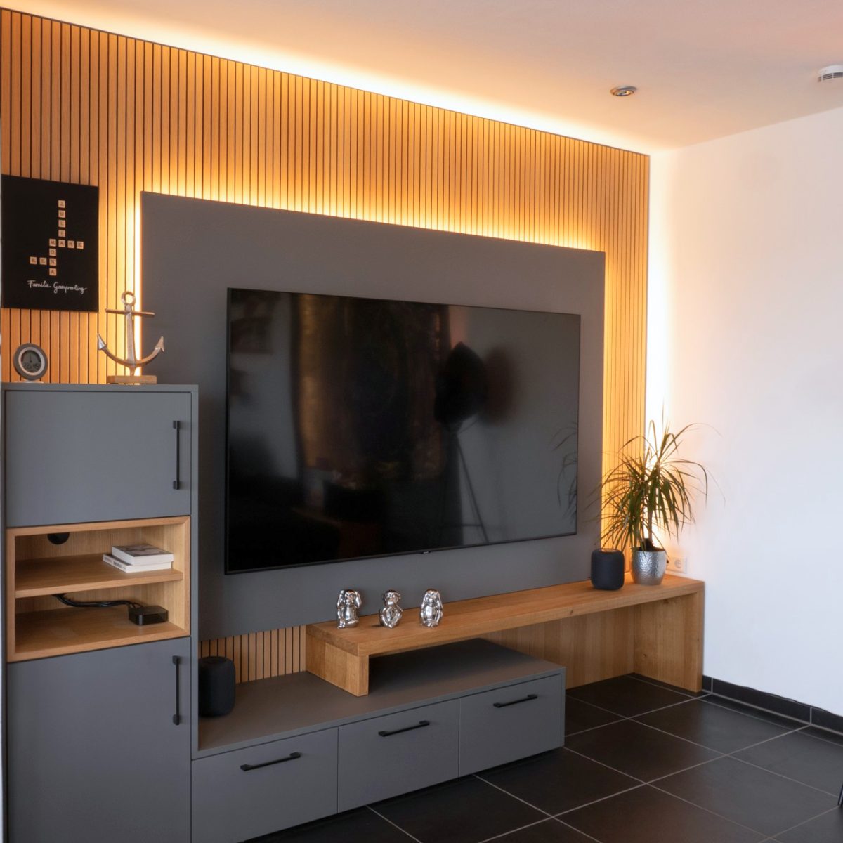 Graues, modernes Sideboard mit Eichenholzeinflüssen vor einer Wand aus warmen Holzpanels mit integrierter Lichtführung, die den Wohnbereich optisch aufwertet.