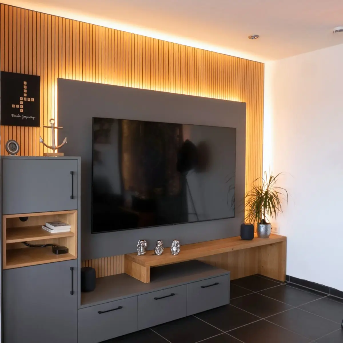 Graues, modernes Sideboard mit Eichenholzeinflüssen vor einer Wand aus warmen Holzpanels mit integrierter Lichtführung, die den Wohnbereich optisch aufwertet.