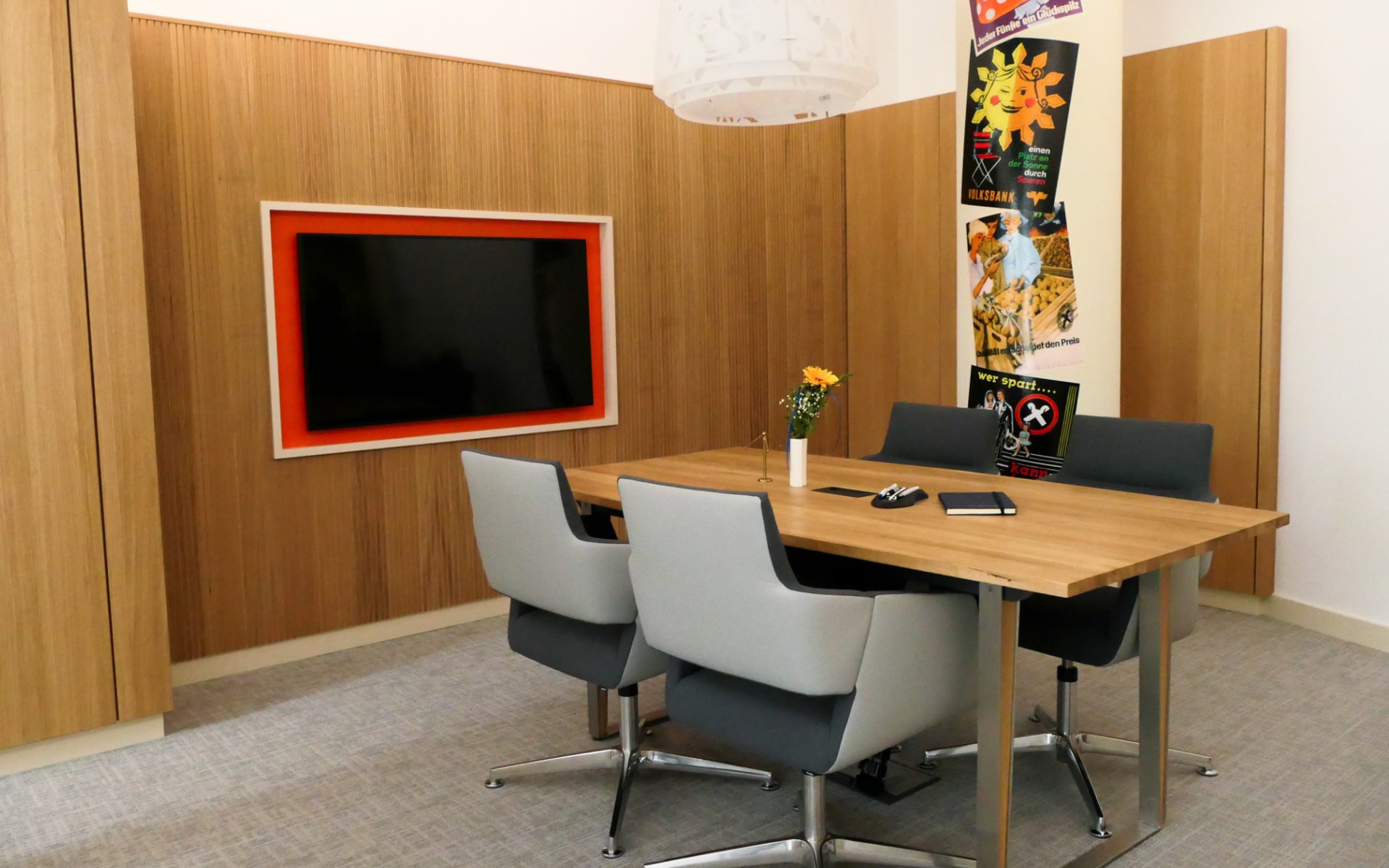 Helles Besprechungszimmer einer Bank mit warmer Eichen‑Holzvertäfelung, großem Eichentisch und vier modernen grauen Stühlen.