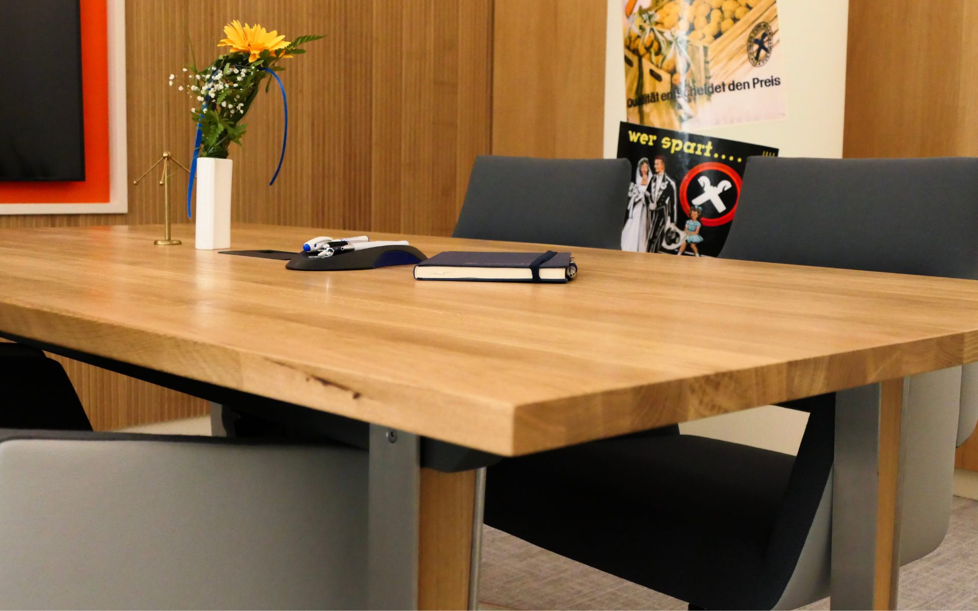 Besprechungsraum mit Eichenholz‑Vertäfelung, großem Eichentisch und grauen Designstühlen, die einen harmonischen Kontrast zwischen warmem Holz und modernen Farben bilden.